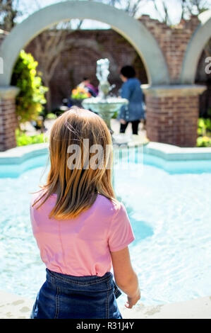 Une jeune fille blonde debout par un écoulement de l'eau fontaine et une brique arbor. Banque D'Images