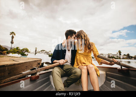 Jeune couple assis dans un bateau de toucher leurs têtes se tenant. Couple sur un bateau ce jour dans un lac siégeant ensemble maintenant les palettes. Banque D'Images