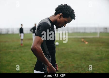 Le joueur de soccer de l'Afrique debout sur un terrain de football à la recherche vers le bas. Vue latérale d'un joueur de football à fatigué debout sur terrain au cours de la pratique. Banque D'Images