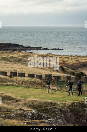 Trois hommes jouer au golf dans un cours par la côte en East Lothian, en Ecosse, avec vue sur la mer en arrière-plan. La verticale Banque D'Images