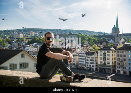 Beau jeune homme s'asseoir dans le parc de la ville avec une vue sur la ville de Zurich en Suisse. Banque D'Images