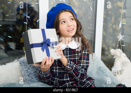 Petite fille mignonne reçu cadeau de vacances. Meilleurs cadeaux de Noël. Enfant heureux de déballer son cadeau. Kid little girl in beret hat tenir fort à l'arc à la maison arrière-plan de la fenêtre. Cadeau de Noël d'ouverture. Banque D'Images