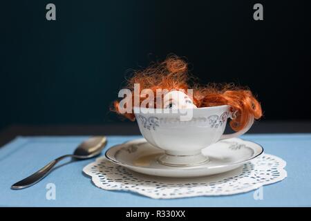 Image surréaliste de poupée à tête rouge dans une tasse de thé. Banque D'Images