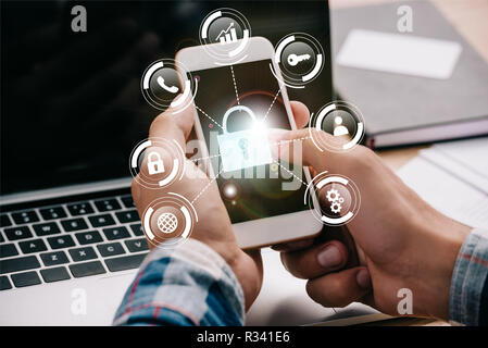 Cropped shot of businessman using smartphone avec signes de sécurité cybernétique sur le lieu de travail avec ordinateur portable Banque D'Images