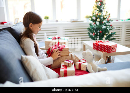 Heureux l'enfant assis sur un canapé et unpacking boxes avec ses cadeaux de Noël Banque D'Images