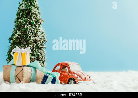 Close-up shot of toy voiture rouge avec des présents et l'arbre de Noël sur la neige permanent fait de coton sur fond bleu Banque D'Images