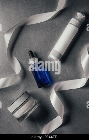 Vue de dessus de la crème de beauté, de sérum et de la lotion entre des rubans argent Banque D'Images
