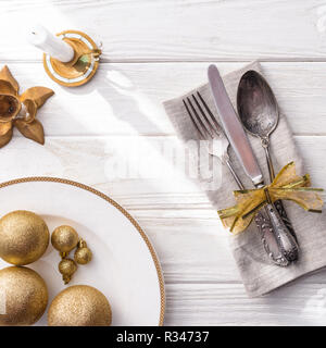 Portrait de plaque avec or boules de Noël, des bougies et de la fourchette, cuillère, couteau enveloppé par ruban sur table en bois Banque D'Images