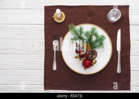 Vue de dessus de table servi avec un verre de vin, assiette, fourchette, couteau, cuillère, bougie et décorations de Noël sur cirée Banque D'Images