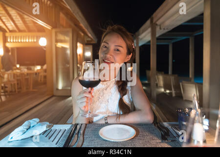 Belle femme asiatique est en train de boire du vin rouge, l'heure du dîner, les restaurants de l'île des Maldives. Banque D'Images