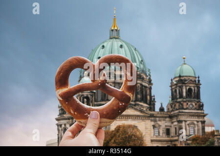 La fille est titulaire d'un délicieux repas traditionnel bretzel allemand dans la main sur la toile de la cathédrale de Berlin est appelé Berliner Dom. Berlin, Allemagne Banque D'Images