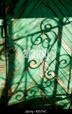 Vieille porte verte ou un mur d'une maison en bois dans un style rustique, avec de la peinture.L'ombre d'une des barres en fer forgé, dessin en noir et blanc Banque D'Images