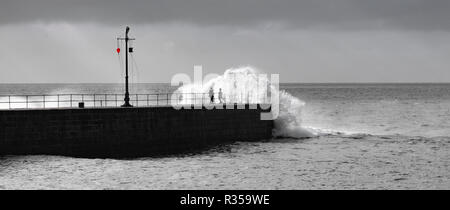 Le noir et blanc avec une seule touche de rouge sur la bouée d'avertissement de suspension au-dessus de personnes obtenant trempé dans d'énormes vagues s'écraser sur le mur du port. Banque D'Images