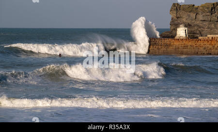 Seul surfer presque perdu dans le fracas des vagues à Portreath Harbour dans le vent et le soleil comme les vagues se briser sur le mur du port. Banque D'Images