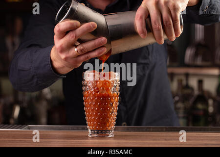 Barman verse rouge tomate jus du shaker, faire un cocktail, un verre au comptoir du bar Banque D'Images