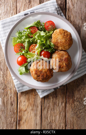 La viande hachée de porc danois savoureuses galettes dans la chapelure avec une salade de légumes frais sur une assiette sur la table. Haut Vertical Vue de dessus Banque D'Images