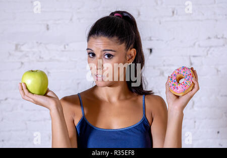 Belle jeune femme inquiète passer faire choix entre Apple et donut dans des aliments mauvais pour la santé, l'alimentation, les calories et detox diet concept. Banque D'Images