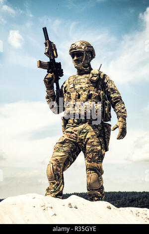 L'homme en uniforme de camouflage militaire et le masque, équipé de munitions tactiques, debout sur dune de sable avec service rifle réplique dans les mains, ciel nuageux sur ba Banque D'Images