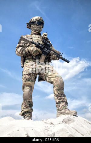 L'homme en uniforme de camouflage militaire et le masque, équipé de munitions tactiques, debout sur dune de sable avec service rifle réplique dans les mains, ciel nuageux sur ba Banque D'Images