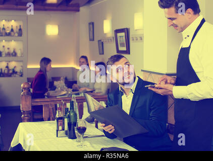 Dans l'ordre positif waiter taking restaurant, aider les jeunes hommes avec menu Banque D'Images