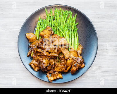 La cuisine chinoise plat - Vue de dessus de la viande dans la sauce de soja frit avec des asperges sur la plaque noire sur le tableau gris Banque D'Images