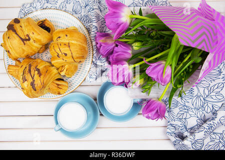 Trois croissants, deux tasses de café sur la table et un bouquet de belles tulipes. Banque D'Images