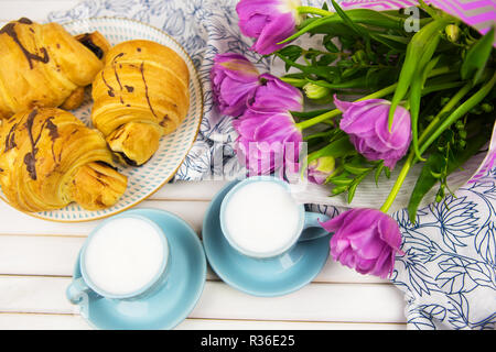 Trois croissants, deux tasses de café sur la table et un bouquet de belles tulipes. Banque D'Images