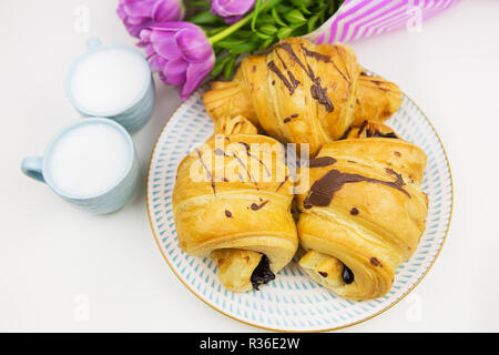 Trois croissants, deux tasses de café sur la table et un bouquet de belles tulipes. Banque D'Images