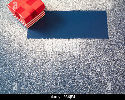 Petit paquet cadeau rouge fort on snowy fond bleu avec la place vide de l'espace de copie de texte pour offrir proposition. high angle shot Banque D'Images