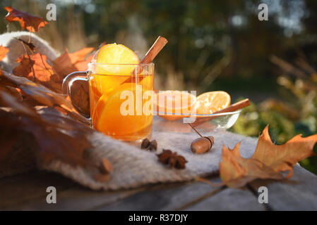 Du thé chaud avec des tranches d'orange et de cannelle sur une table de jardin en bois avec une couverture et les feuilles d'automne, l'espace de copie sélectionné, la mise au point, la profondeur de champ étroite Banque D'Images