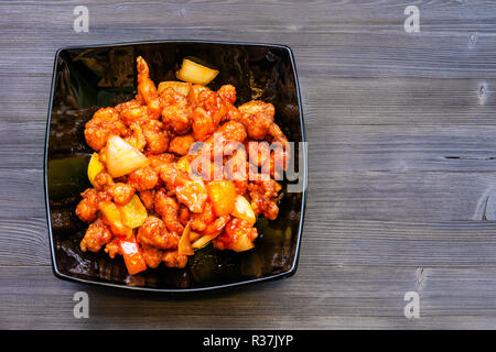 La cuisine chinoise plat - Vue de dessus des morceaux de poulet frit à l'ananas et le poivron et l'oignon (Poulet aigre-doux) en noir sur bol en bois Banque D'Images