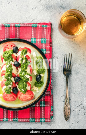 Salade caprese tomate et mozzarella et pesto aux olives de table gris servi avec serviette et verre rouge contrôlée vin blanc ou jus de pomme fourchette. Banque D'Images