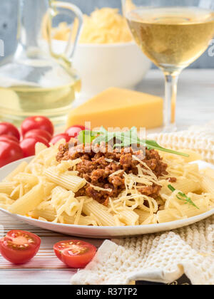 Les pâtes italiennes Penne bolognaise rigatone la viande hachée à la sauce tomate et de parmesan. Nature morte sur table en bois blanc, servi avec des tomates cerises, Banque D'Images