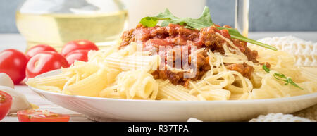 Les pâtes italiennes Penne bolognaise rigatone la viande hachée à la sauce tomate et de parmesan. Nature morte sur table en bois blanc, servi avec des tomates cerises, Banque D'Images