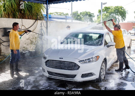 Miami Florida,Little Havana,lavage de voiture,blanc Ford Fusion,homme hispanique hommes,travail,nettoyage,tuyau d'eau pulvérisation haute pression,travail d'équipe,FL18111 Banque D'Images