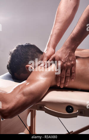 Vue de côté, deux jeune homme, 20-29 ans, physiothérapie sportive à l'intérieur en studio, séance photo. Masser l'épaule physiothérapeute patient avec son ha Banque D'Images