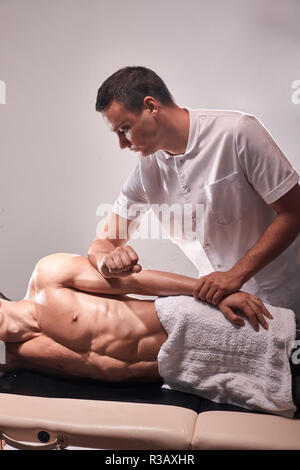 Deux jeune homme, 20-29 ans, physiothérapie sportive à l'intérieur en studio, séance photo. Bras de massage masseur thérapeute patient musculaire portant sur sa Banque D'Images