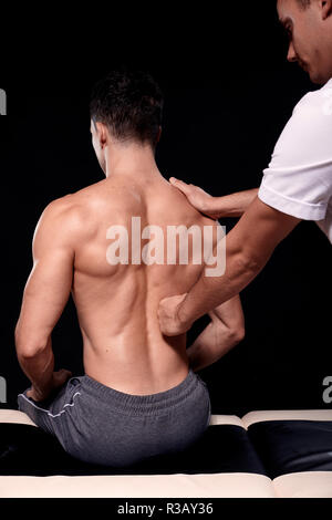 Deux jeunes hommes, de 20 à 29 ans. physiothérapeute patients massage dos musclé avec son poing, vue arrière. studio shot, fond noir. Banque D'Images