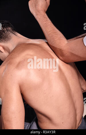 Deux jeunes hommes, de 20 à 29 ans. physiothérapeute patients massage dos musclé avec son coude, vue arrière, close-up. studio shot, fond noir. Banque D'Images