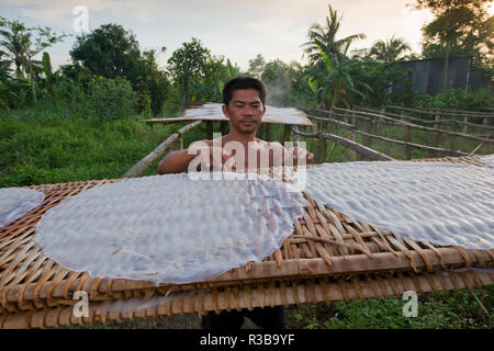 Travailleur vietnamien s'étend de nouilles de riz à la vapeur les galettes sur cadre en bambou pour sécher, usine de nouilles de riz, Delta du Mékong, Cần Thơ Banque D'Images