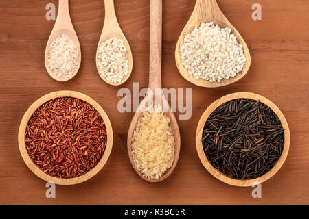 Une collection de divers types de riz, tourné par le haut sur un fond de bois rustique foncé avec copie espace. Rouge, noir sauvage, à grains, la paella, le risotto Banque D'Images