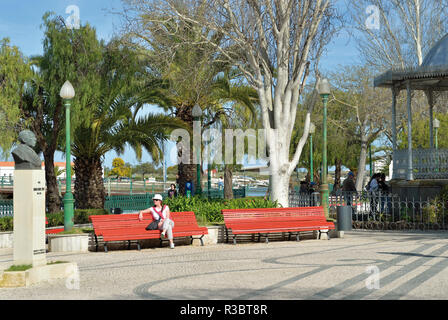 Woman sitting on park bench rouge dans un cadre idyllique de la Vieille-Ville enjoying sun Banque D'Images