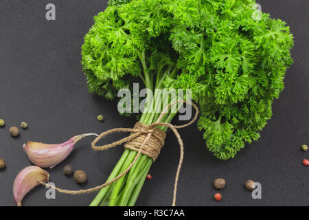 Un bouquet de persil frais bandé avec une corde avec un arc et un mélange d'épices et l'ail sur un tableau noir, vue du dessus Banque D'Images