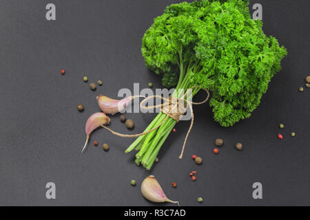 Un bouquet de persil frais bandé avec une corde avec un arc et un mélange d'épices et l'ail sur un tableau noir, vue du dessus Banque D'Images