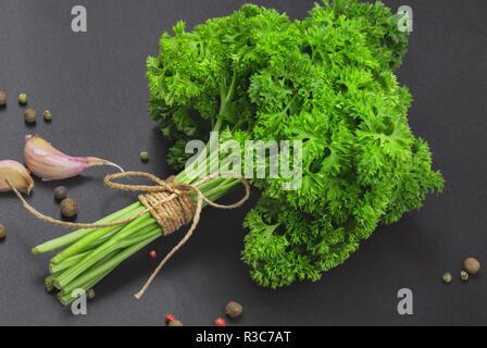 Un bouquet de persil frais bandé avec une corde avec un arc et un mélange d'épices et l'ail sur un tableau noir, vue du dessus Banque D'Images