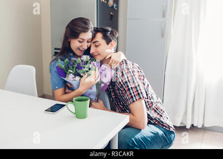 Jeune homme gifting bouquet de fleurs à sa petite amie dans la cuisine. Heureux couple hugging. Surprise romantique à la maison Banque D'Images