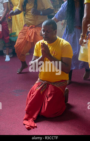 Un hindou pieux adorateur sur ses genoux avec les mains jointes dans un temple hindou dans le Queens, New York. Banque D'Images