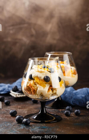 Maison saine layered dessert trifle à l'orange, myrtille, biscuit, yaourt et granola dans un des verres. Place pour le texte Banque D'Images