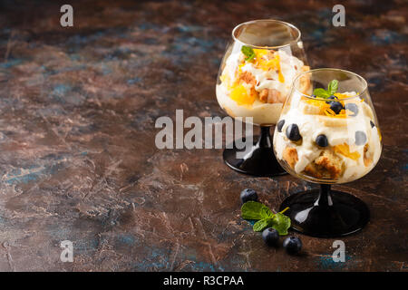 Deux verres à couches maison saine dessert trifle à l'orange, de bleuet, de biscuits, de yaourts et de muesli. Place pour le texte Banque D'Images