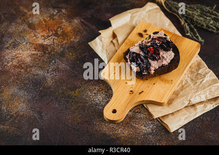 Sandwich avec patee canard et les prunes séchées sur une planche à découper en bois, de l'huile d'olive, sel, poivre, ail et branches de thym sur un fond sombre. Espace pour t Banque D'Images